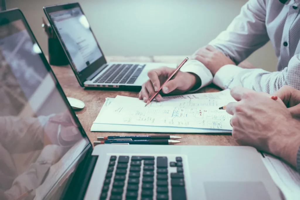 Two professionals reviewing property management documents at a desk with laptops during a consultation